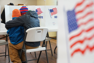 A voter fills out a ballot at the Spiritual Renewal Center with a child on their lap.